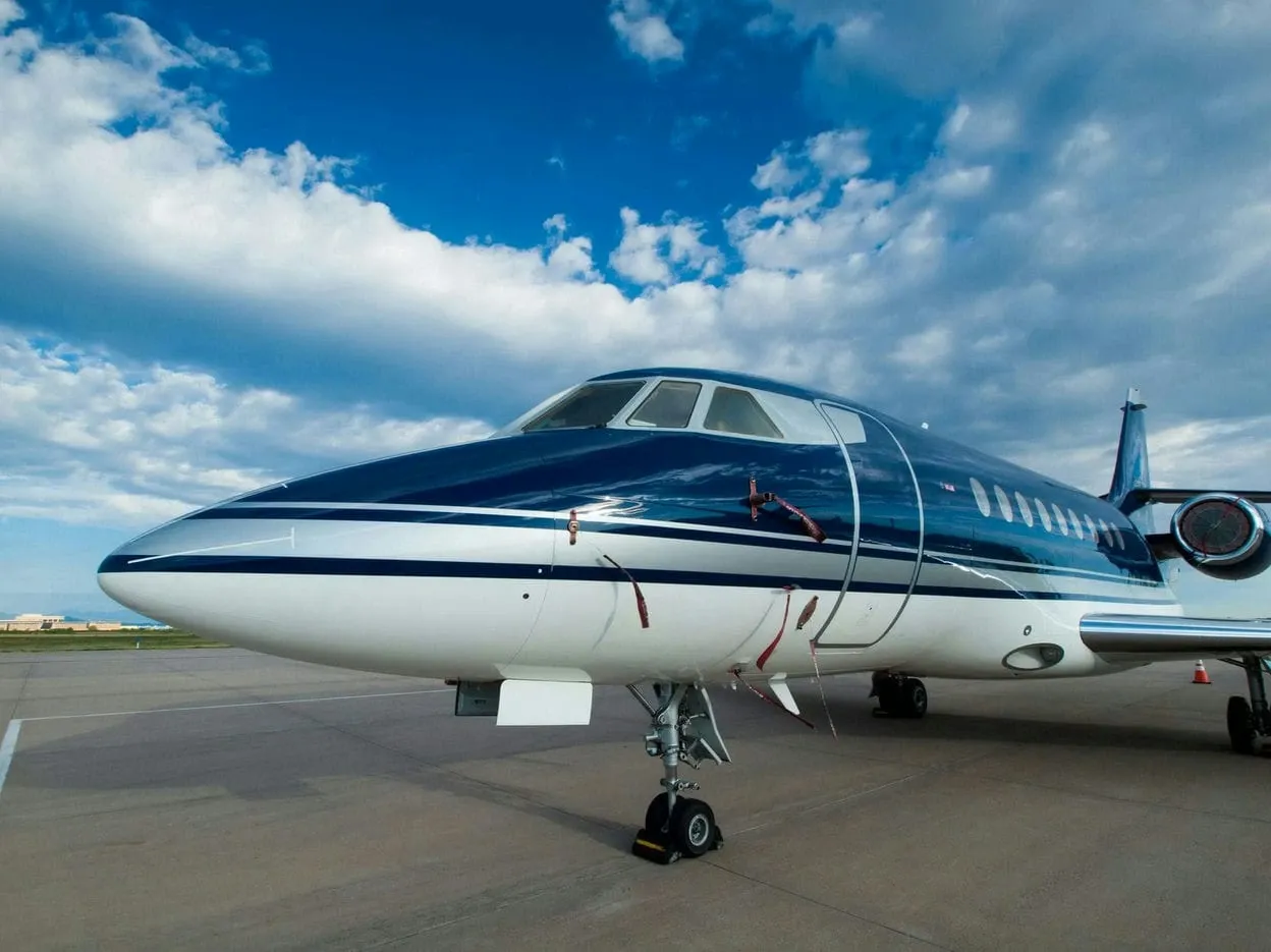 Private jet with navy blue stripe parked on tarmac under a blue sky with clouds