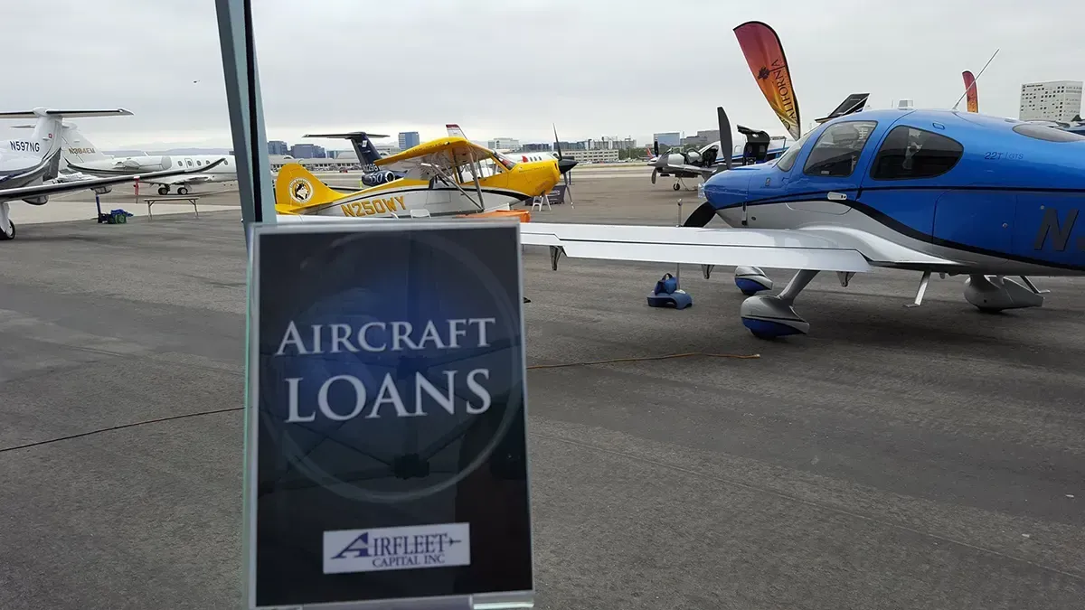 Airfield showcasing a lineup of small aircraft, including a sign in the foreground that reads "Aircraft Loans" with the logo of Airfleet Capital, Inc.