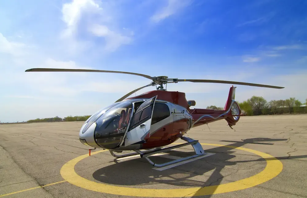 Red and white private helicopter parked on a yellow helipad circle under a blue sky